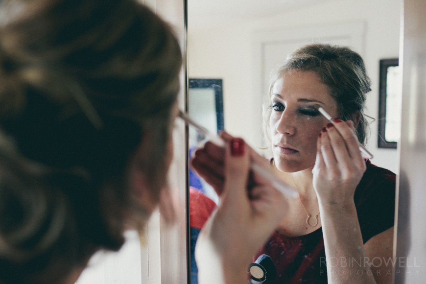 A bridesmaid applies makeup while looking in the mirror