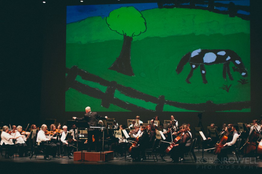 A large screen shows a backdrop of a child's painting behing the orchestra