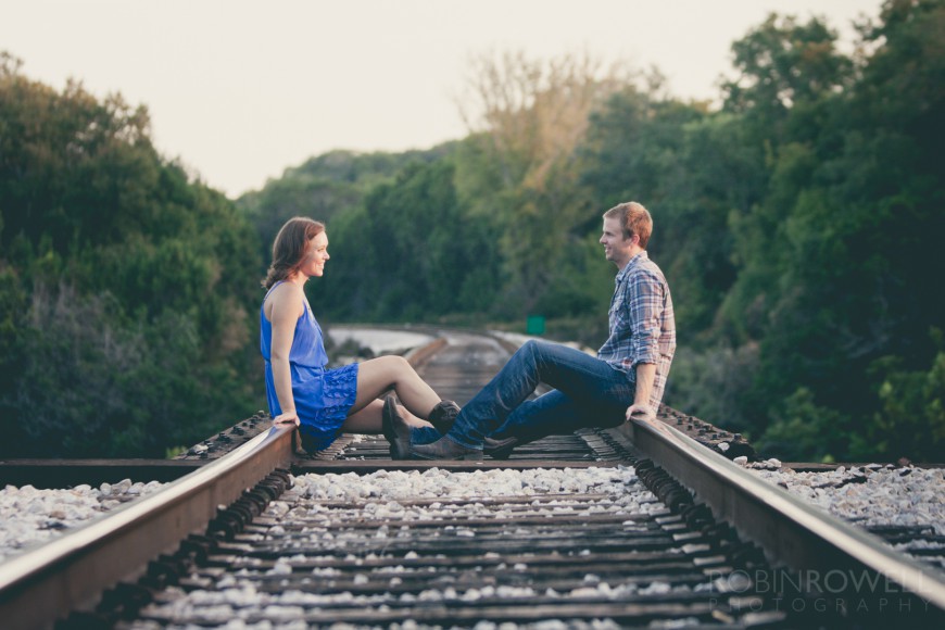 Boone and Aubrey face each other sitting on railroad tracks