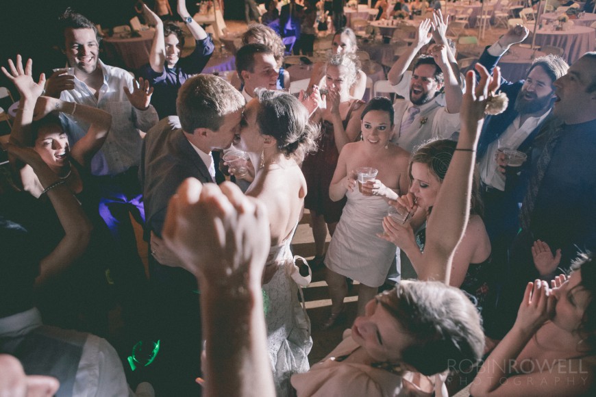 The bride and groom embrace and kiss within the crowd of cheering onlookers - ranch style wedding in Leander, TX