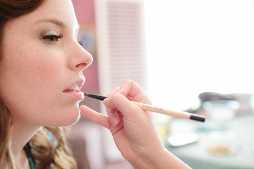 Lip gloss is carefully applied to the bride's lips