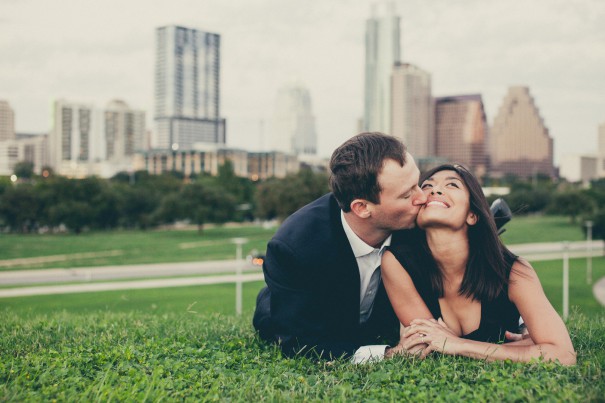 Paul and Marianne share a kiss on a grassy hill overlooked the Austin, TX downtown skyline - engagement photo by Robin Rowell