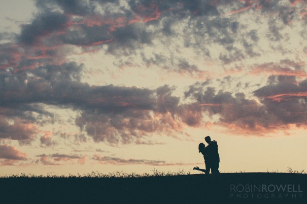 Marianne and Paul are silhouetted against puffy clouds during an Austin fall sunset.  Engagement photo by Robin Rowell Photography  