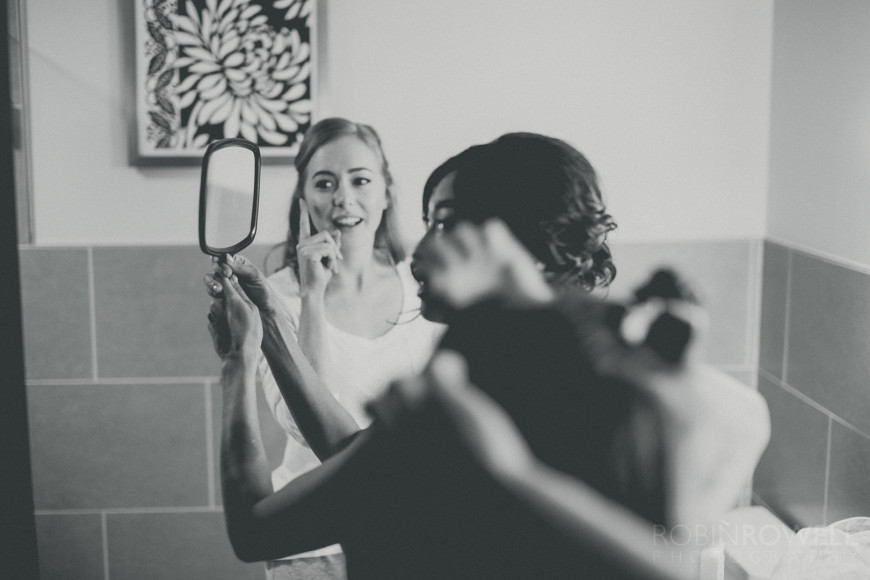 The bridesmaids look on as the bride examines her hair in a handheld mirror