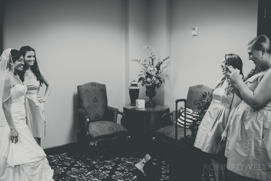 A black and white photo of bridesmaids taking snapshots of the bride